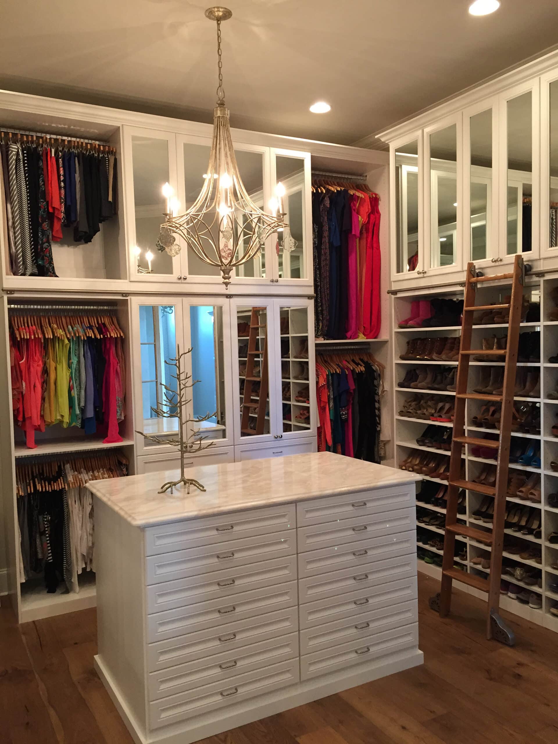 Walk-in closet with white shelving, mirrors framed in white and a library ladder