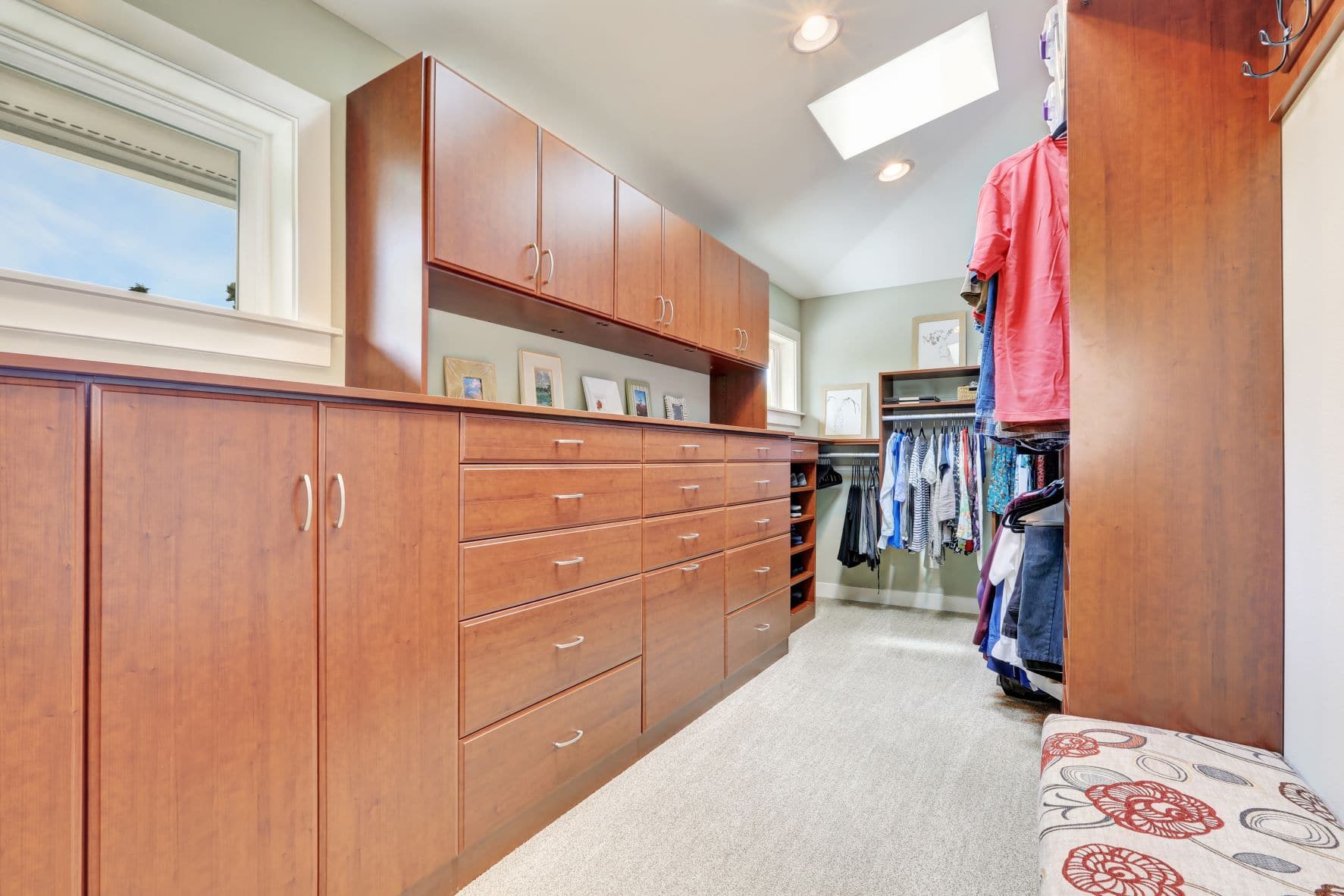 A large walk-in closet with medium-colored wood and a seating area