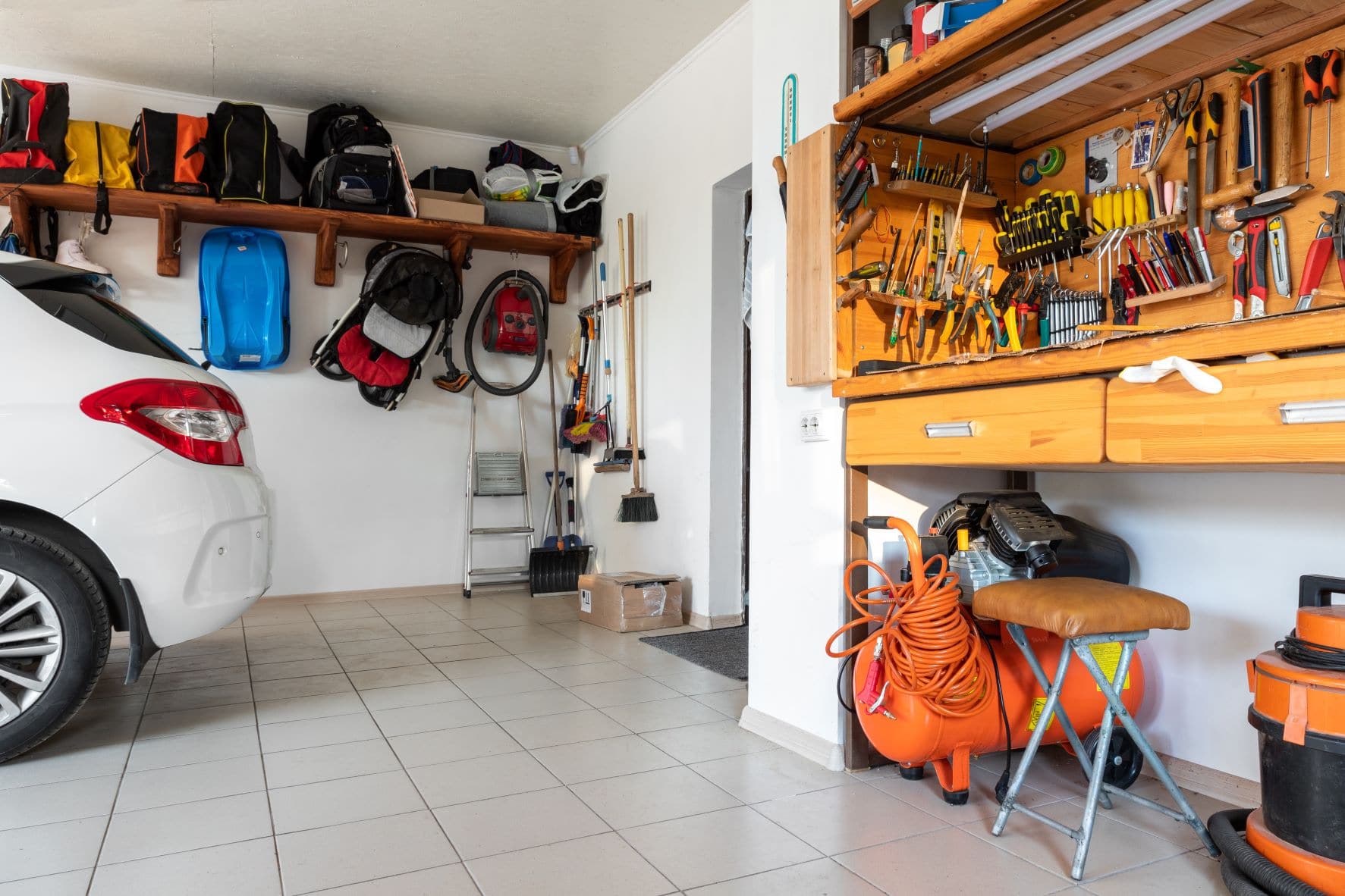 A garage with a tile floor and extensive organized storage for tools and bags