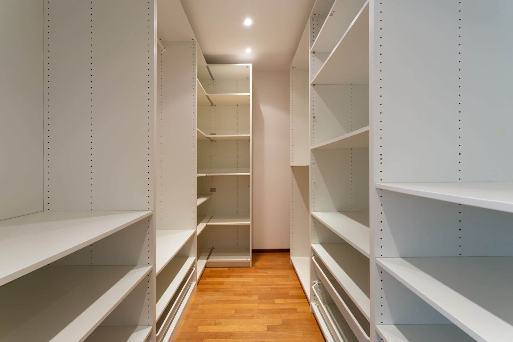 Large new walk-in closet with white shelving and wood flooring