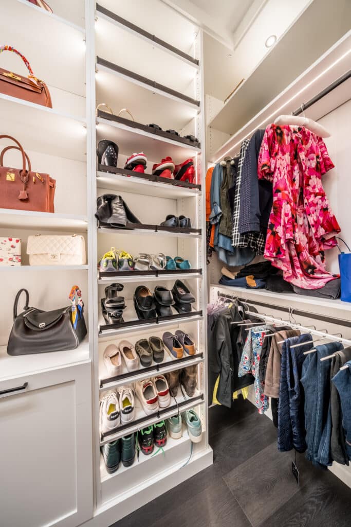 a well lit luxury closet with white shelves that is full of colorful clothes